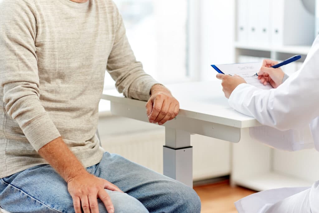 Shown from the neck down, a casually-dressed man discusses concierge medicine with his physician