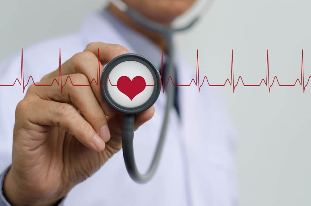 A doctor holds up a stethoscope with a glowing heart superimposed at its center, surrounded by animated EKG waveforms radiating outward