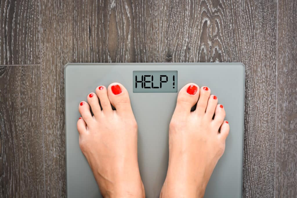 A woman's feet, standing on a scale that says "HELP" on the display panel